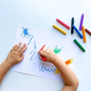 small child draws with pastel crayons on white table. High quality photo